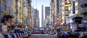 Una calle en Buenos Aires en la cual se ve una carretera edificios a los lados y el obelisco al fondo